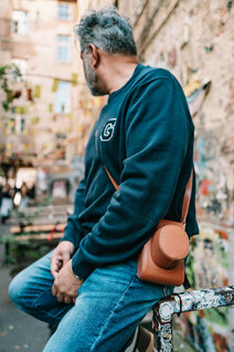 Mann sitzt auf Geländer mit Oberwerth Crossbody Holster aus Leder, Streetart im Hintergrund