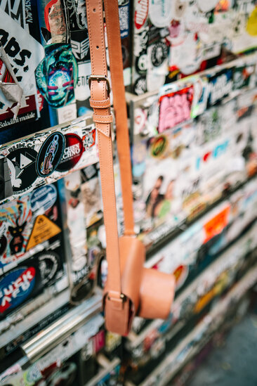 Mann trägt Oberwerth Crossbody Holster vor Sticker-Wand, Jeans und Pullover