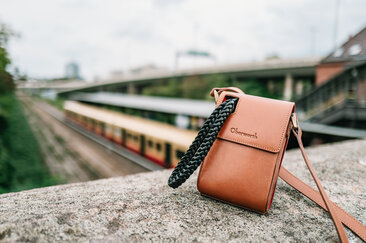 Oberwerth Crossbody Holster aus Leder auf Steinmauer mit unscharfer S-Bahn im Hintergrund